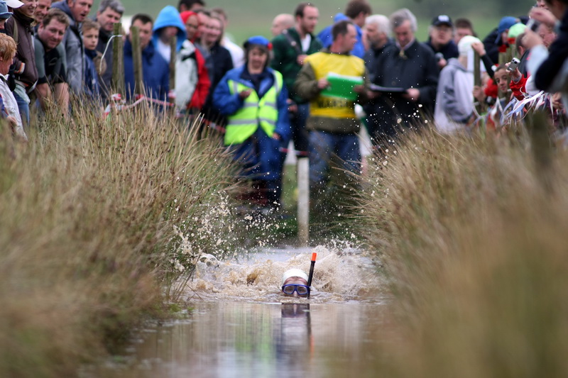 Bog snorkeling competitor in wetsuit and snorkel completing a length of the peat bog trench in Wales