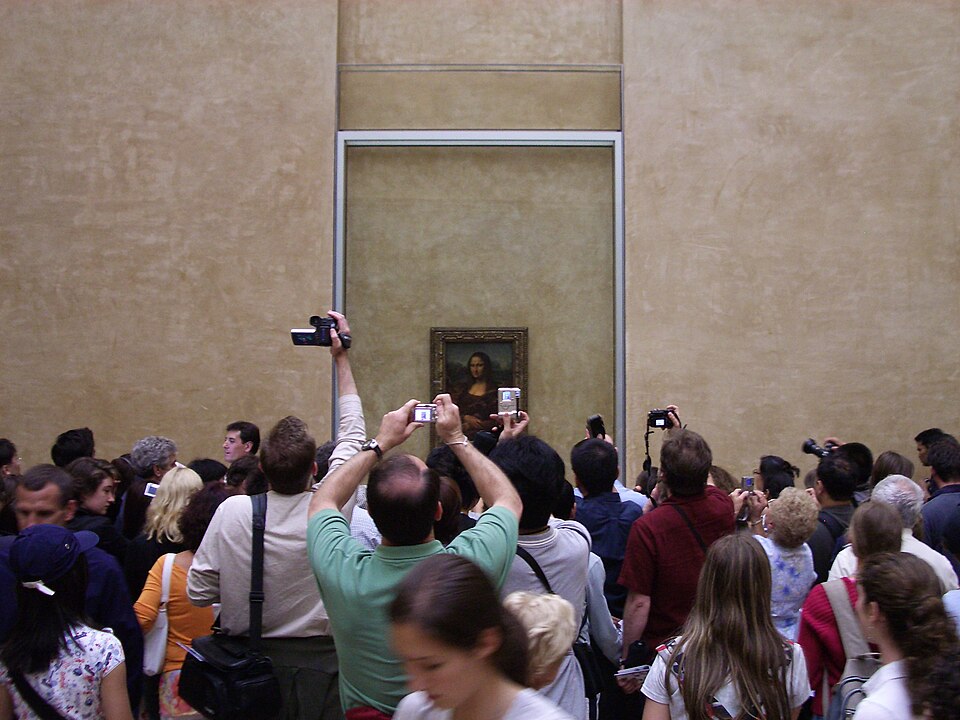 Crowds of visitors photographing the Mona Lisa from behind the Louvre's exclusion barrier