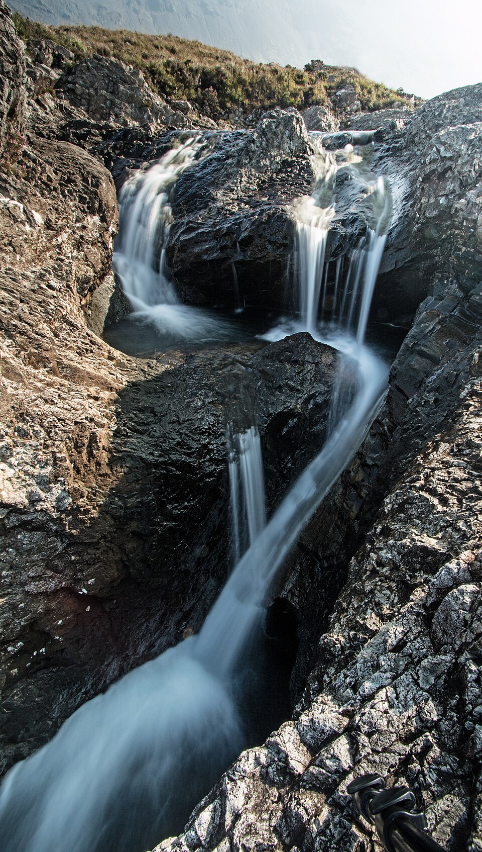 The Fairy Pools on the Isle of Skye, clear turquoise water running between rocky outcrops with misty mountains behind