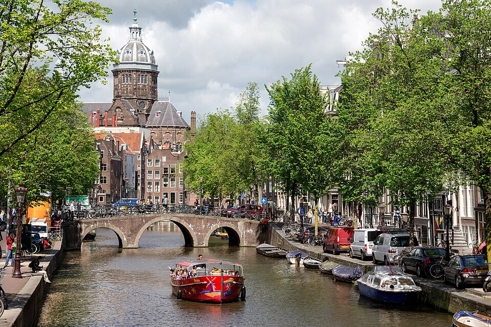 Long boat passing through an Amsterdam canal flanked by the city's tall narrow gabled houses