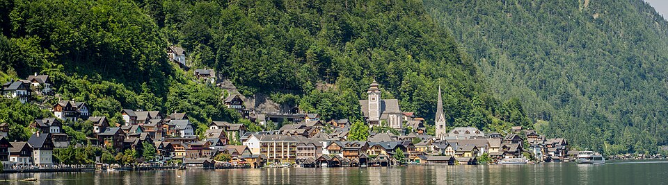 Pastel houses and a white church spire reflected in the still alpine lake at Hallstatt, Austria