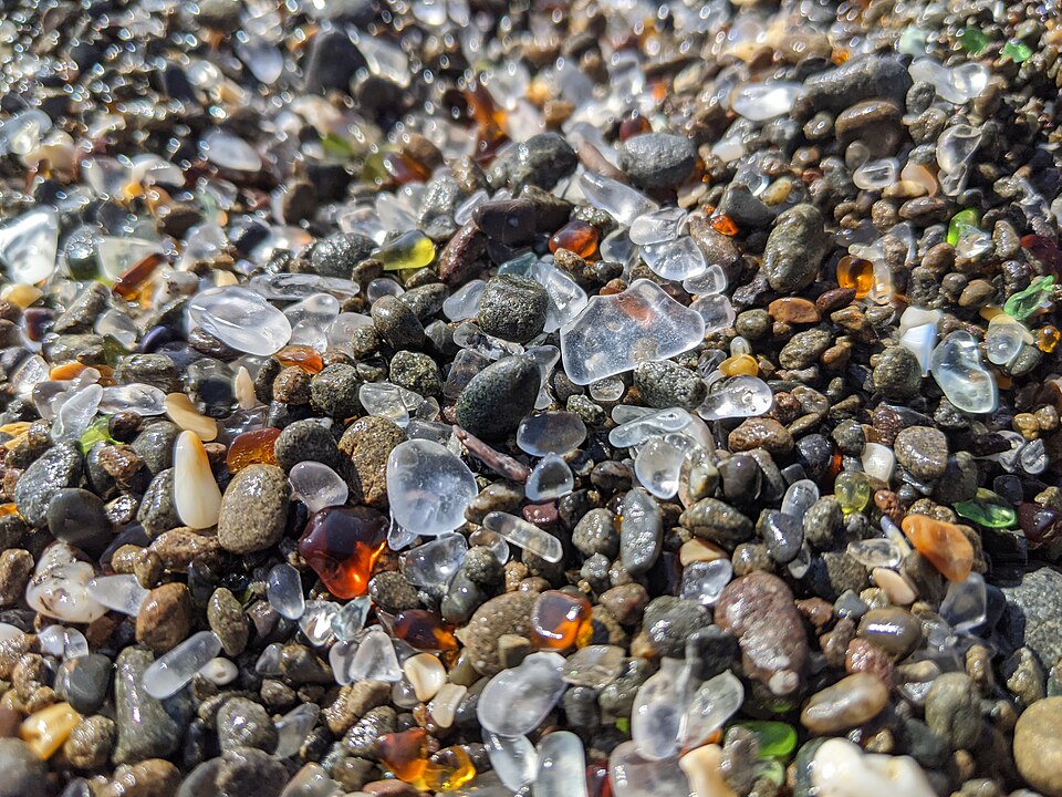 Smooth sea-tumbled glass pebbles in white, amber and green mixed with stones at Glass Beach in Fort Bragg, California
