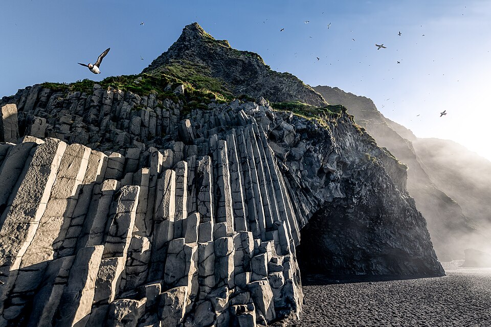 Hexagonal basalt columns and black volcanic sand at Reynisfjara beach near Vik on the south coast of Iceland, with seabirds overhead