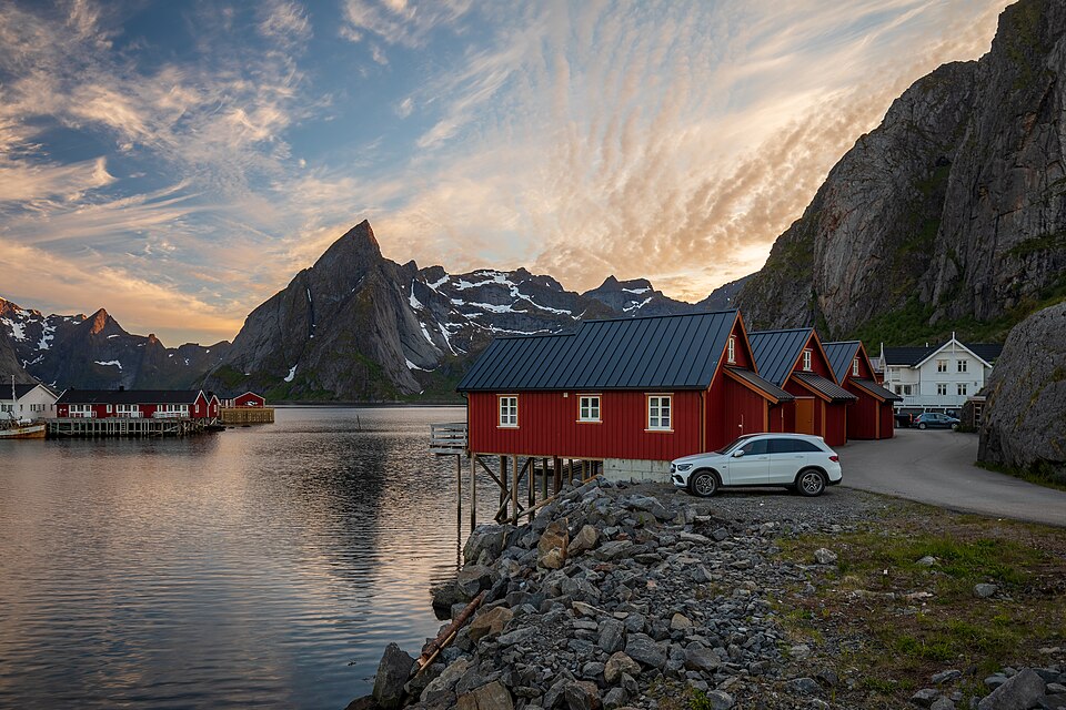 Red rorbuer fishing cabins on stilts beside the water at Reine in the Lofoten Islands, Norway, under low golden Arctic light