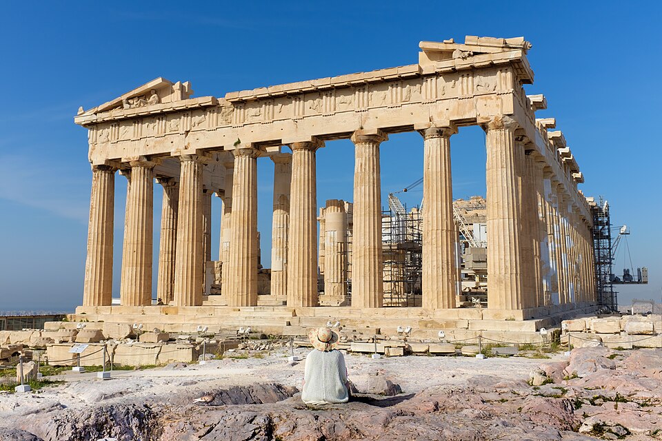 Visitors walking on the Acropolis of Athens with the Parthenon visible against a clear blue sky