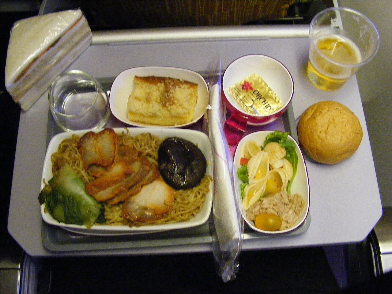 Inflight meal tray on Thai Airways with multiple plastic-covered components - airline meals undergo multiple reheating cycles that can dramatically alter food textures